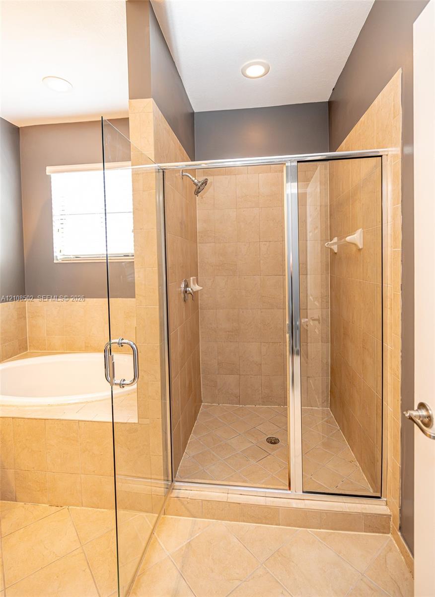 Shower enclosure with glass paneling, tile-surround tub deck, neutral wall tiling, and recessed ceiling lighting