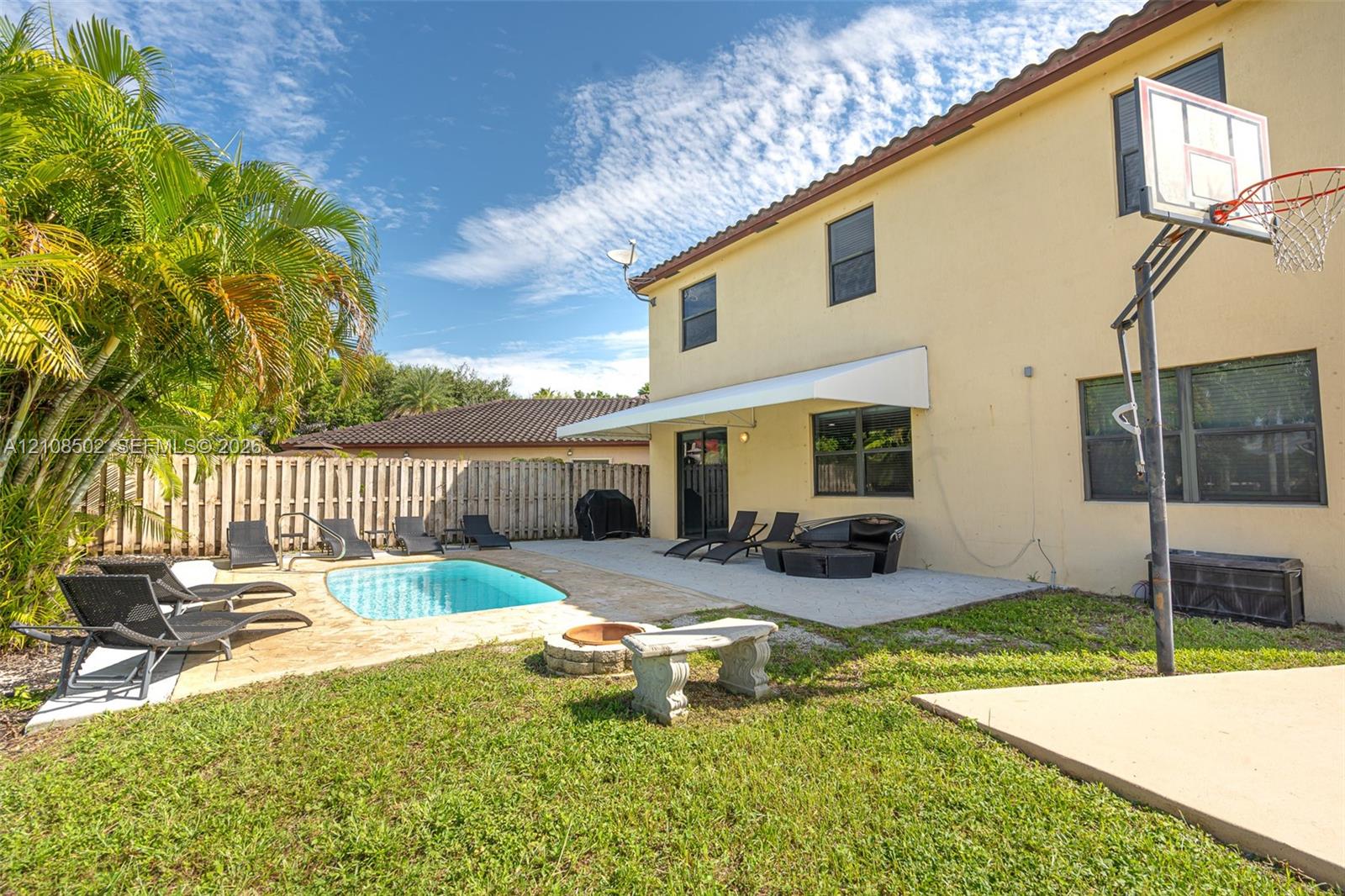 Exterior space featuring a concrete patio, in-ground swimming pool, stone fire pit, and a concrete sports pad