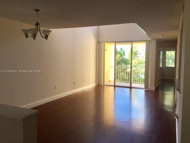 Living area featuring vaulted ceilings, wood-finish flooring, a multi-arm chandelier, and sliding glass doors opening to a private balcony Living area featuring vaulted ceilings, wood-finish flooring, a multi-arm chandelier, and sliding glass doors opening to a private balcony