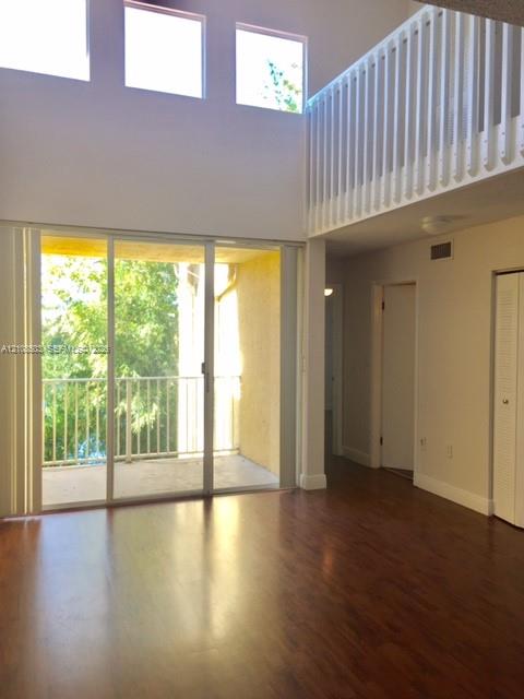 Double-height living area featuring wood-finish flooring, floor-to-ceiling sliding glass doors, upper-level interior balcony railing, and clerestory windows Double-height living area featuring wood-finish flooring, floor-to-ceiling sliding glass doors, upper-level interior balcony railing, and clerestory windows