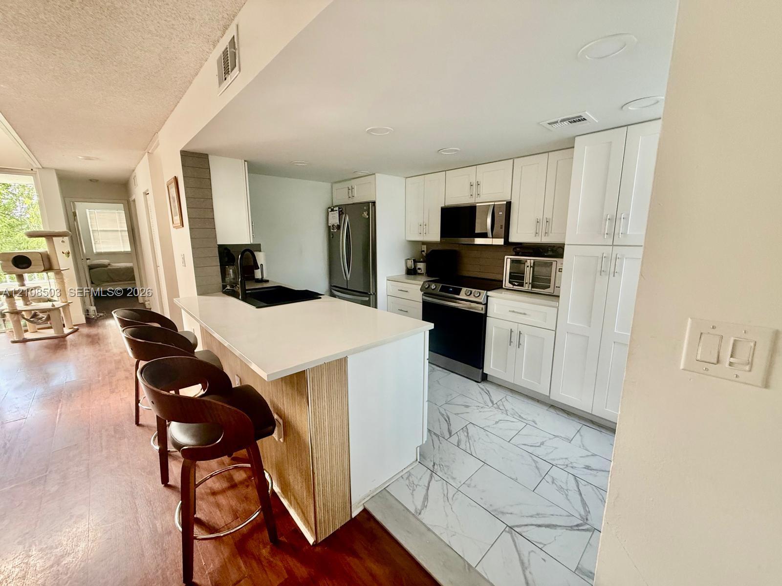 Kitchen featuring white shaker-style cabinetry, a stone-finish countertop peninsula, stainless steel appliances, and large-format tile flooring