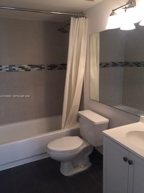 Bathroom featuring a bathtub with tile surround and decorative glass mosaic inlay, vanity with integrated basin, large wall-mounted mirror, and multi-bulb vanity lighting Bathroom featuring a bathtub with tile surround and decorative glass mosaic inlay, vanity with integrated basin, large wall-mounted mirror, and multi-bulb vanity lighting
