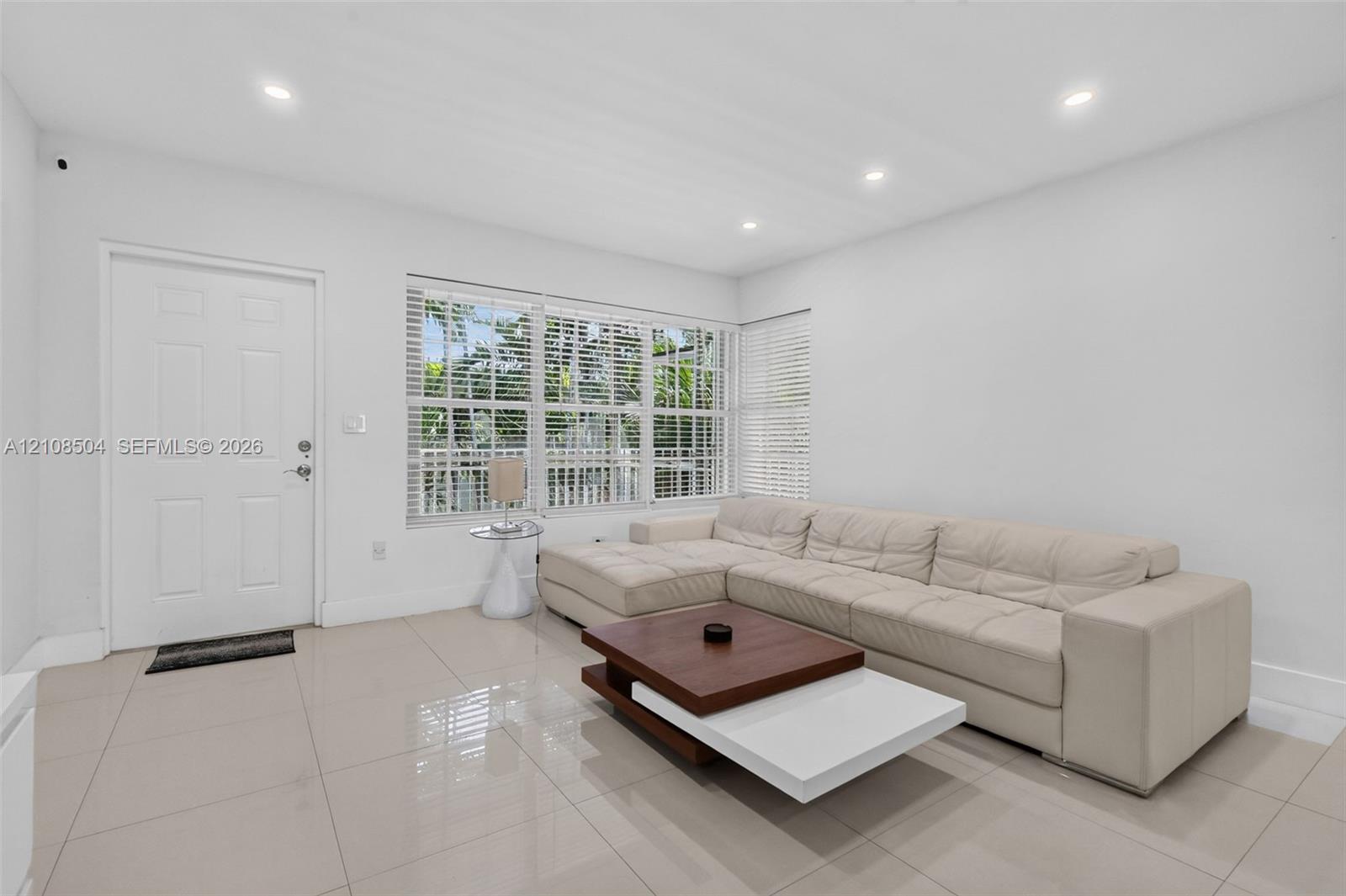 Large-format neutral tile flooring, recessed ceiling lighting, and expansive windows fitted with horizontal blinds