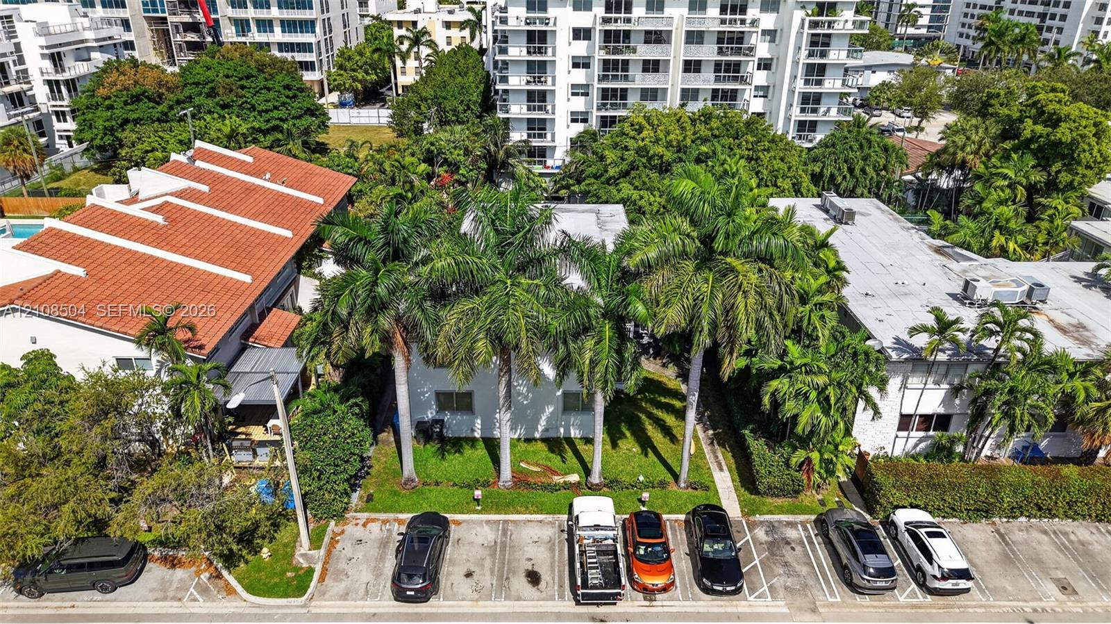 Aerial perspective featuring a multi-story building with a flat roof, mature palm trees, and designated surface parking
