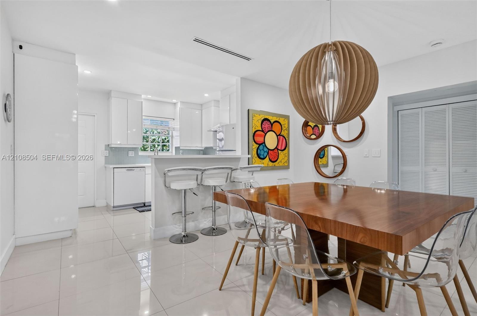 Kitchen featuring high-gloss cabinetry, stone-finish countertops, porcelain tile flooring, and a breakfast bar, complemented by a statement spherical wood-slat pendant light