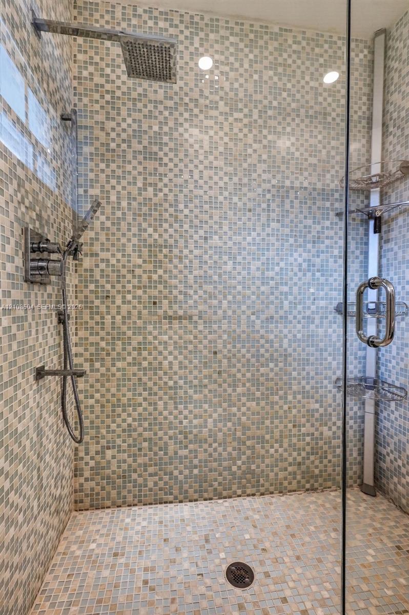 Walk-in shower featuring glass enclosure, mosaic tile wall surround, rainfall showerhead, handheld sprayer, and built-in corner shelving