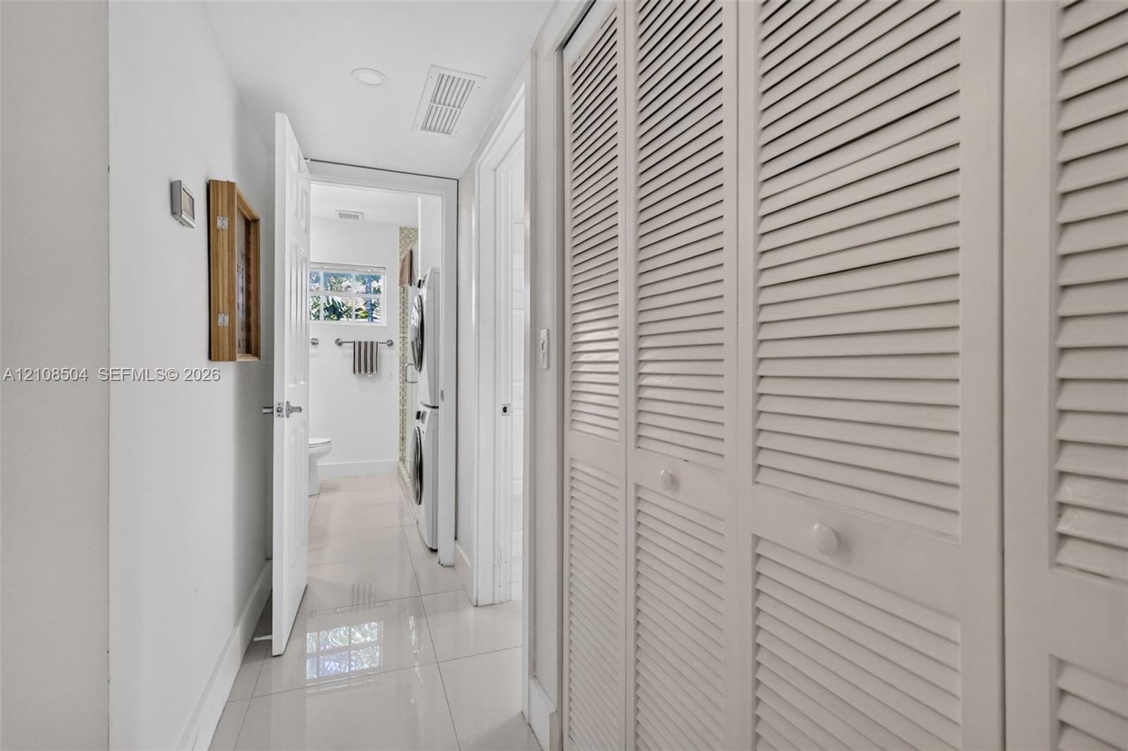 Hallway featuring full-height louvered closet doors, polished tile flooring, and recessed ceiling lighting