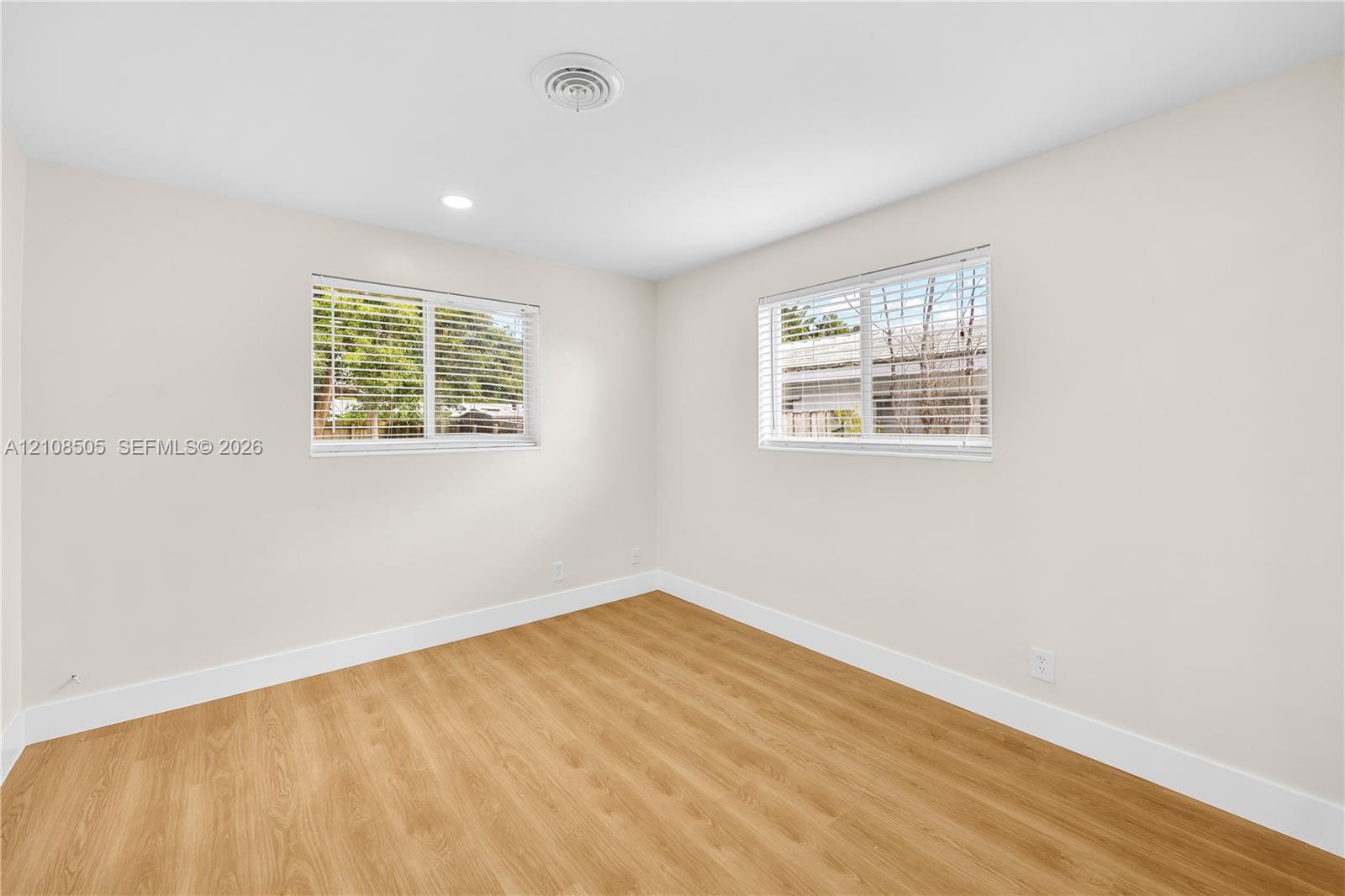 Neutral interior space featuring wood-finish flooring, dual windows with horizontal blinds, and recessed ceiling lighting