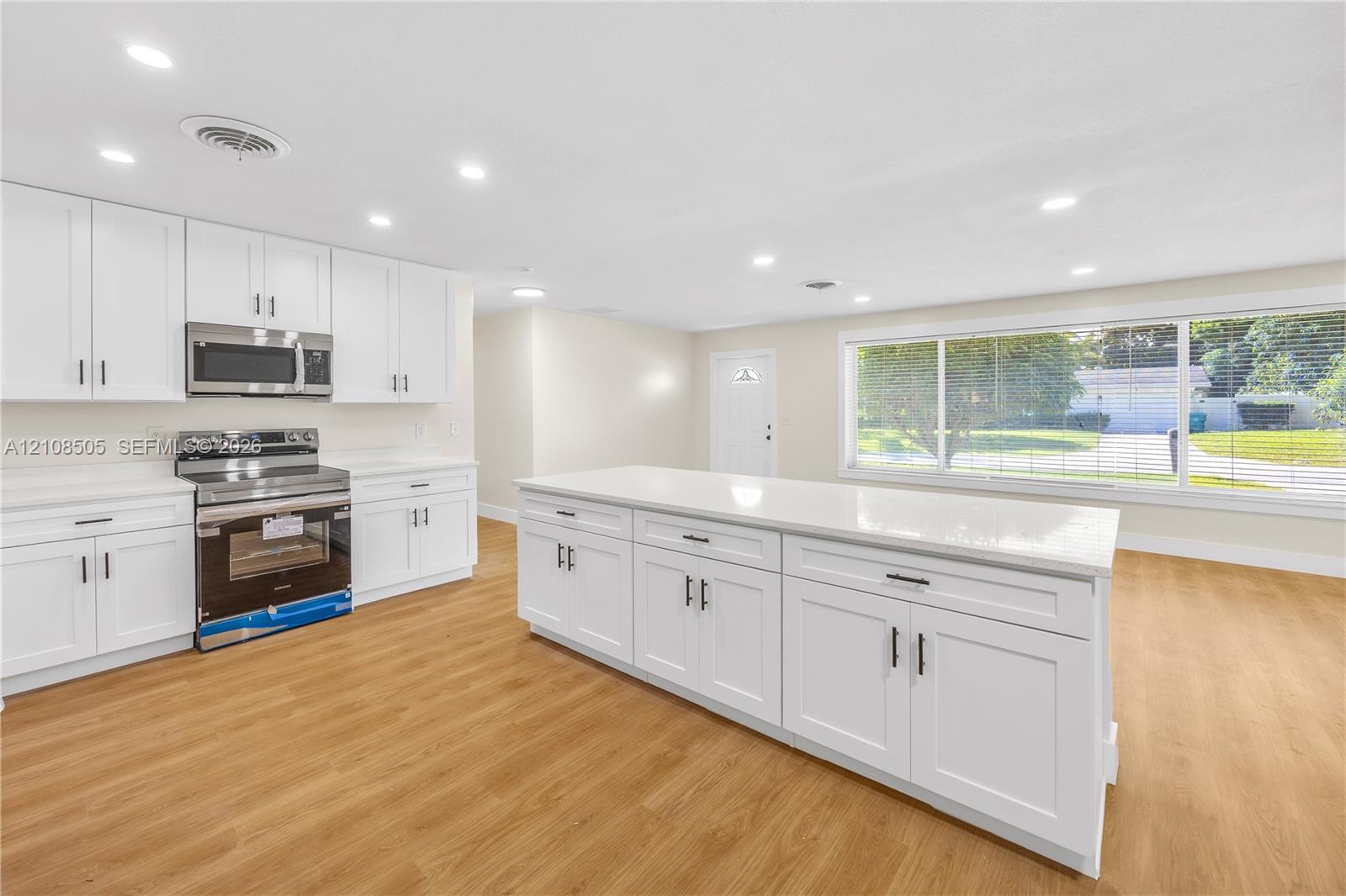 Kitchen featuring white shaker-style cabinetry, a quartz-topped center island, wood-finish flooring, recessed lighting, and stainless steel appliances