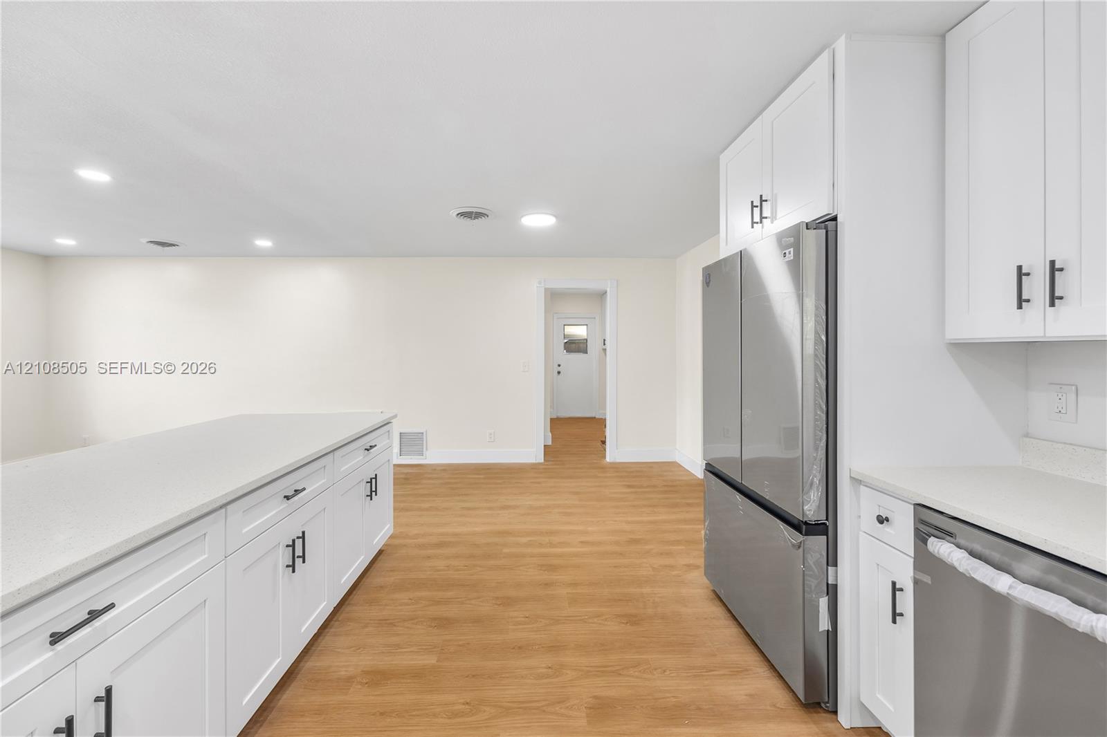 Kitchen featuring white shaker-style cabinetry, solid-surface countertops, wood-finish flooring, and stainless steel appliances