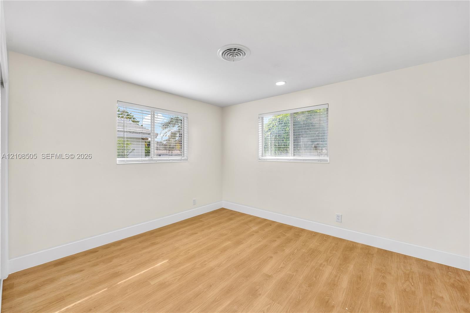 Neutral-toned interior featuring wood-finish flooring, recessed lighting, and dual windows with horizontal blinds