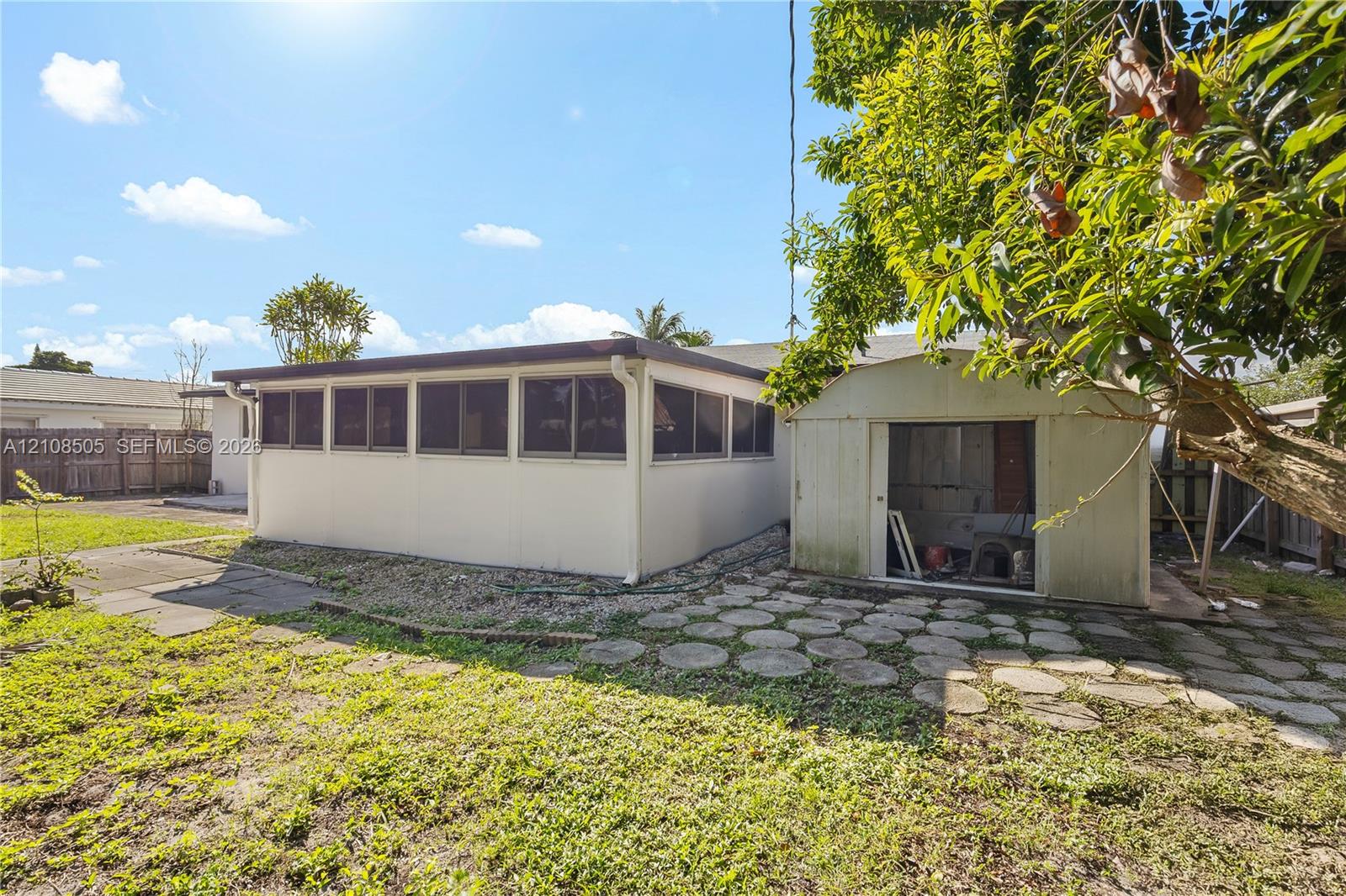 Enclosed porch with multiple windows, concrete paver patio, standalone storage structure, and perimeter wood fencing