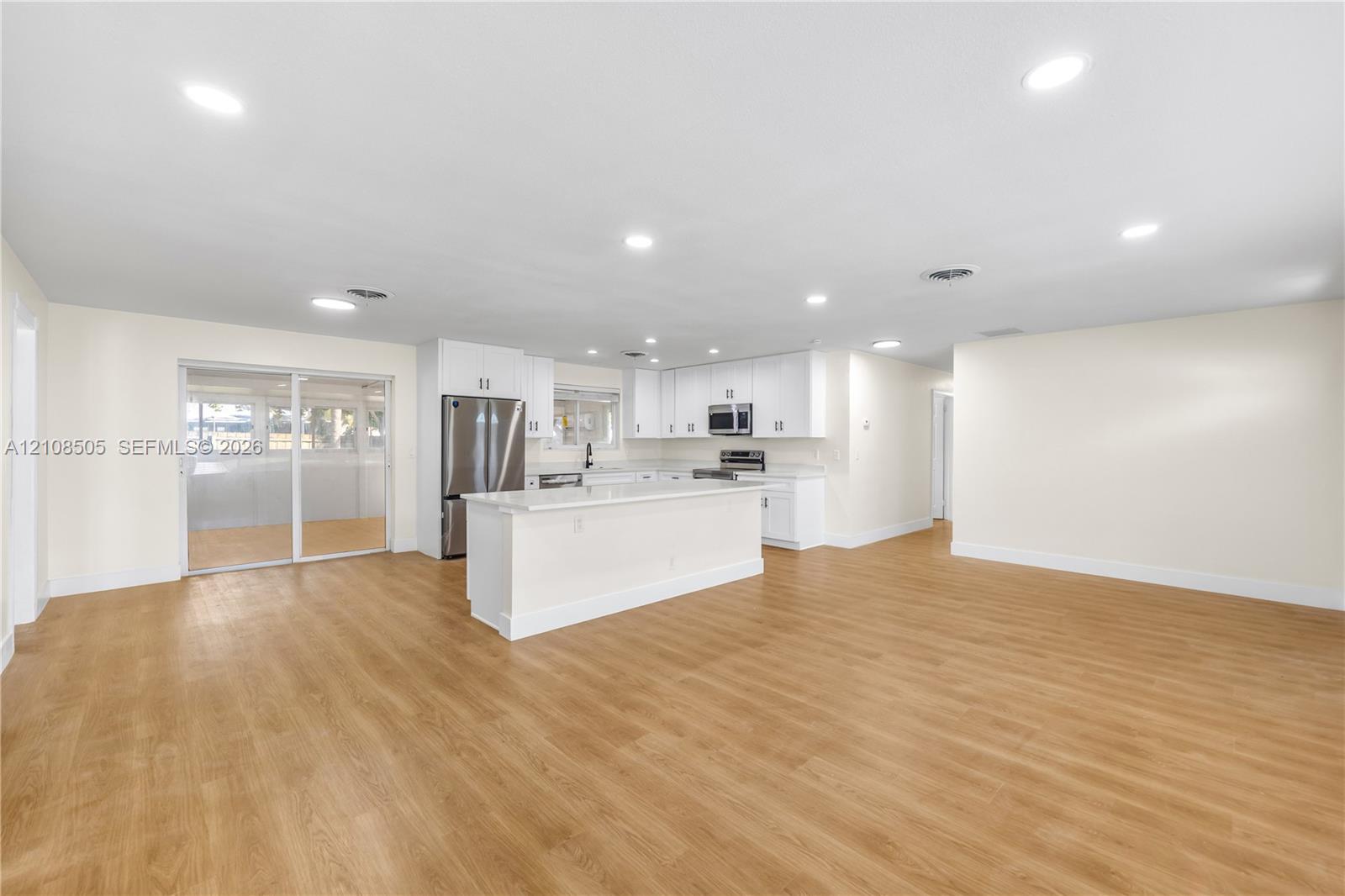 Open-concept kitchen featuring white shaker-style cabinetry, quartz countertops, a center island, stainless steel appliances, and wood-finish flooring Open-concept kitchen featuring white shaker-style cabinetry, quartz countertops, a center island, stainless steel appliances, and wood-finish flooring