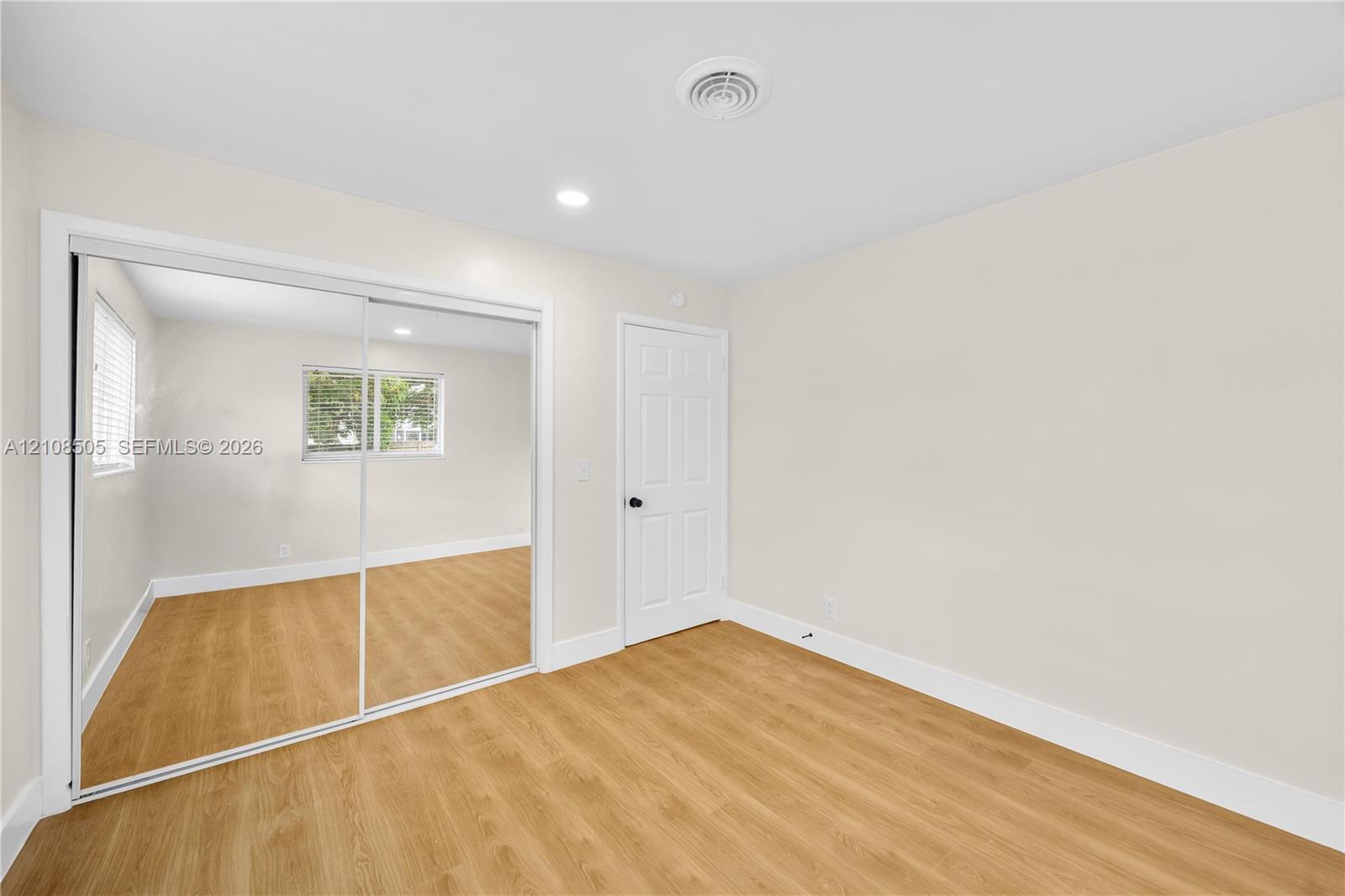 Room featuring wood-finish flooring, sliding mirrored closet doors, and a paneled interior door