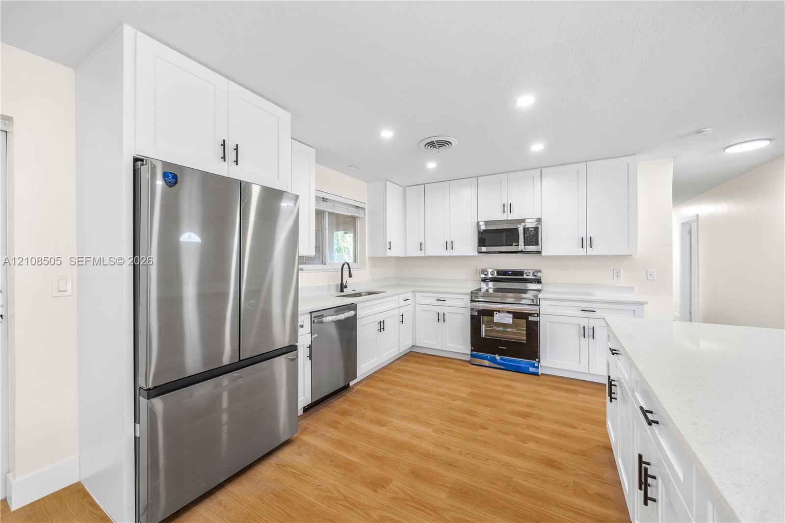 Kitchen featuring white shaker-style cabinetry, solid-surface countertops, wood-finish flooring, stainless steel appliances, and recessed lighting