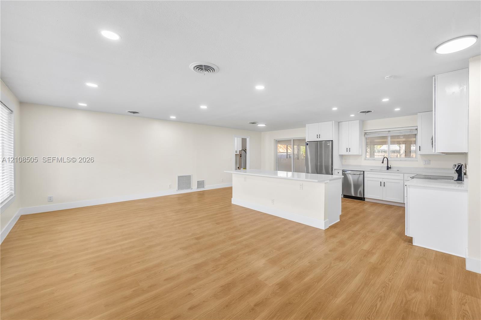 Open-concept interior featuring wood-finish flooring, recessed lighting, and a kitchen equipped with white cabinetry, quartz countertops, and a stainless steel refrigerator Open-concept interior featuring wood-finish flooring, recessed lighting, and a kitchen equipped with white cabinetry, quartz countertops, and a stainless steel refrigerator