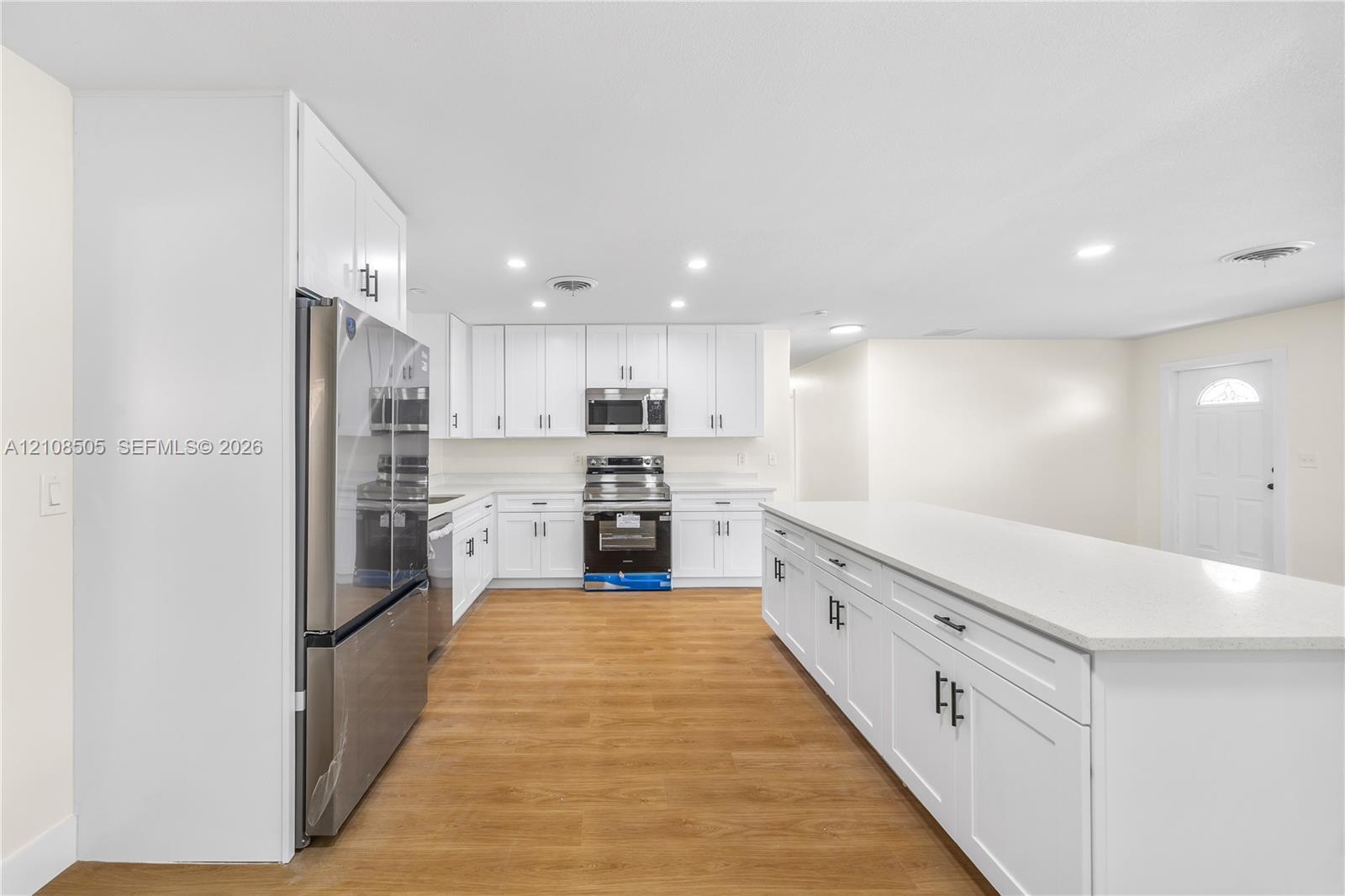 Kitchen featuring white shaker-style cabinetry, quartz countertops, a large central island, stainless steel appliances, and wood-finish flooring