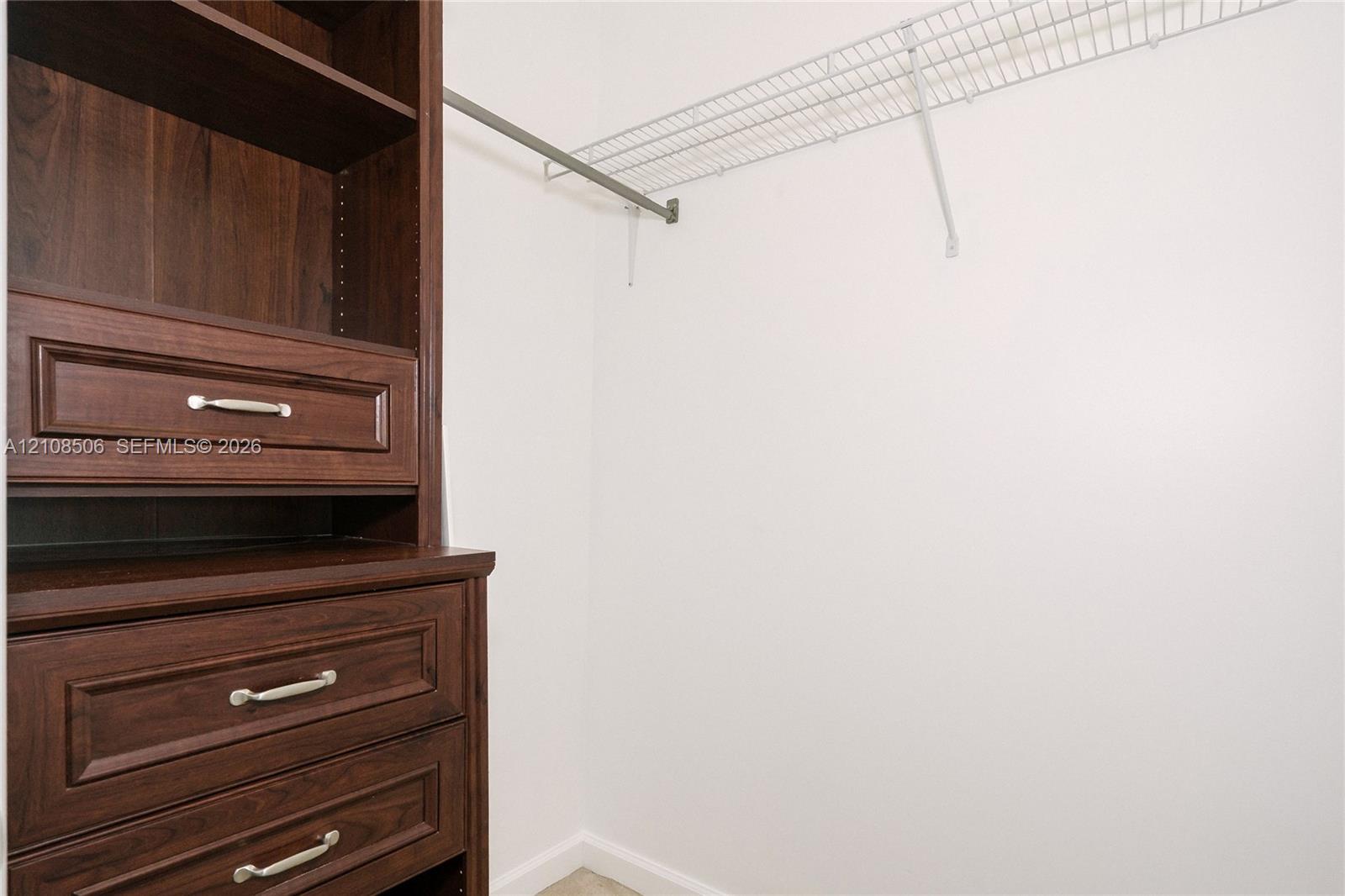 Built-in wood-finish shelving unit with three drawers featuring metallic hardware, paired with an overhead metal closet rod and wire shelving