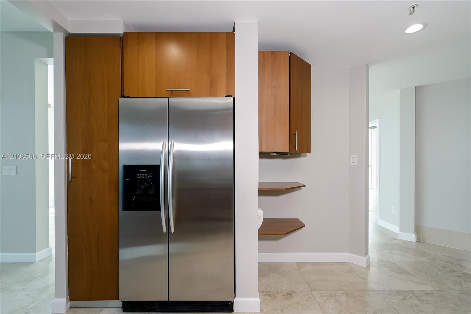 Stainless steel side-by-side refrigerator, wood-finish cabinetry with vertical hardware, custom built-in shelving, and tile flooring