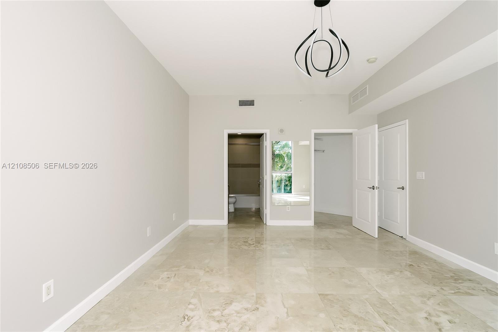 Neutral-toned room featuring large-format tile flooring, modern sculptural pendant lighting, and multiple interior door entries with panel detailing