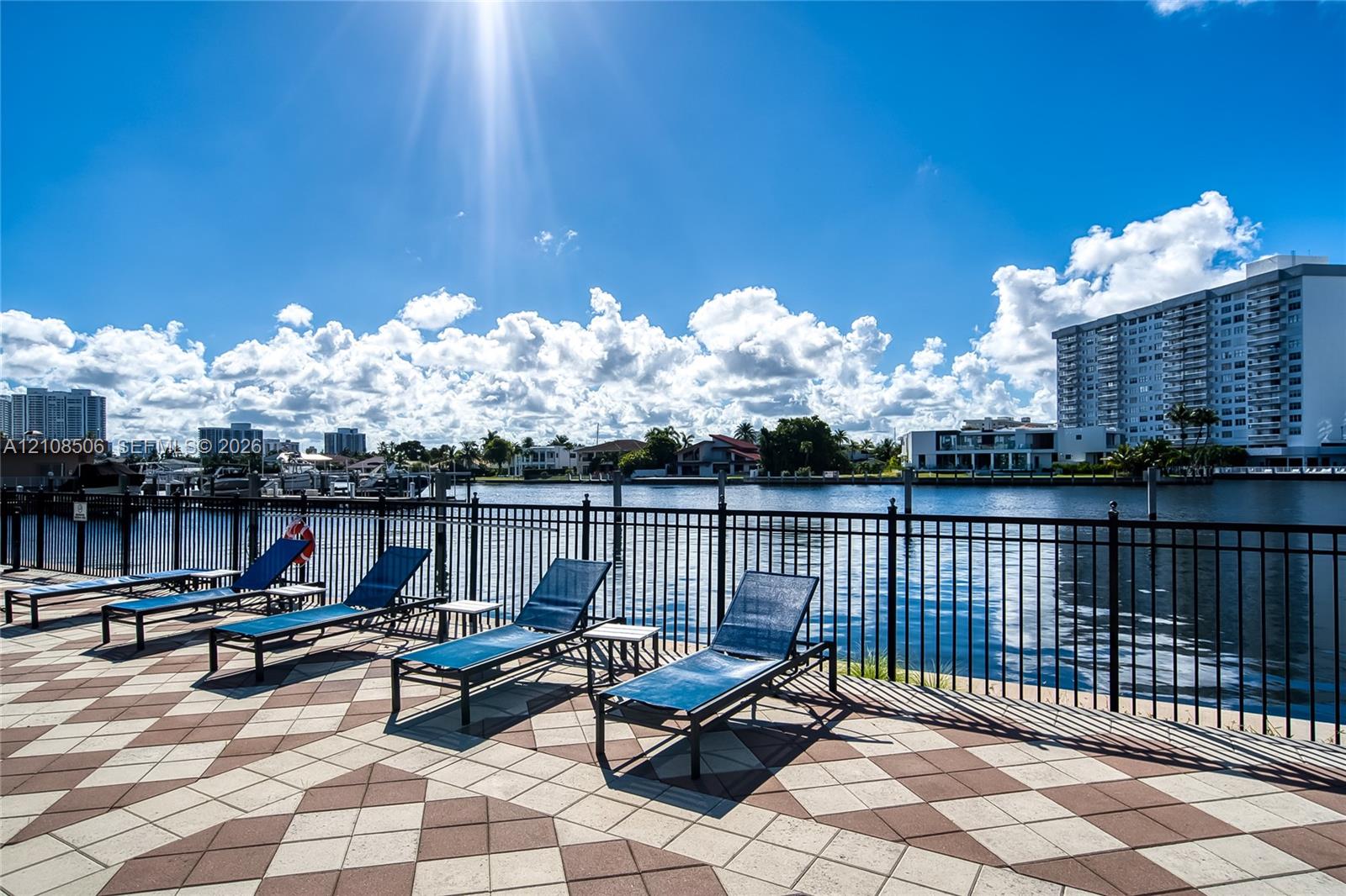 Waterfront terrace featuring a geometric tile patio, black metal perimeter fencing, and bulkhead dockage