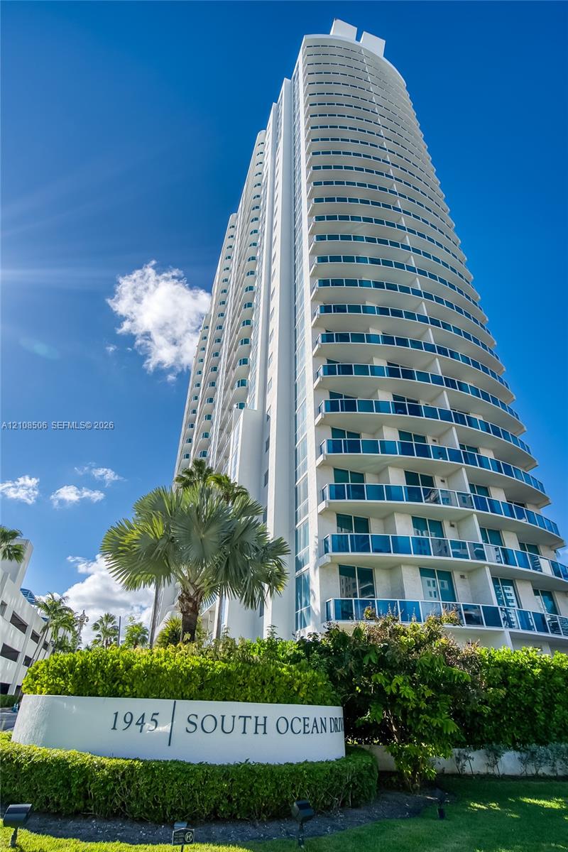 High-rise tower featuring tiered glass balconies, smooth white facade, and landscaped grounds with mature palm trees