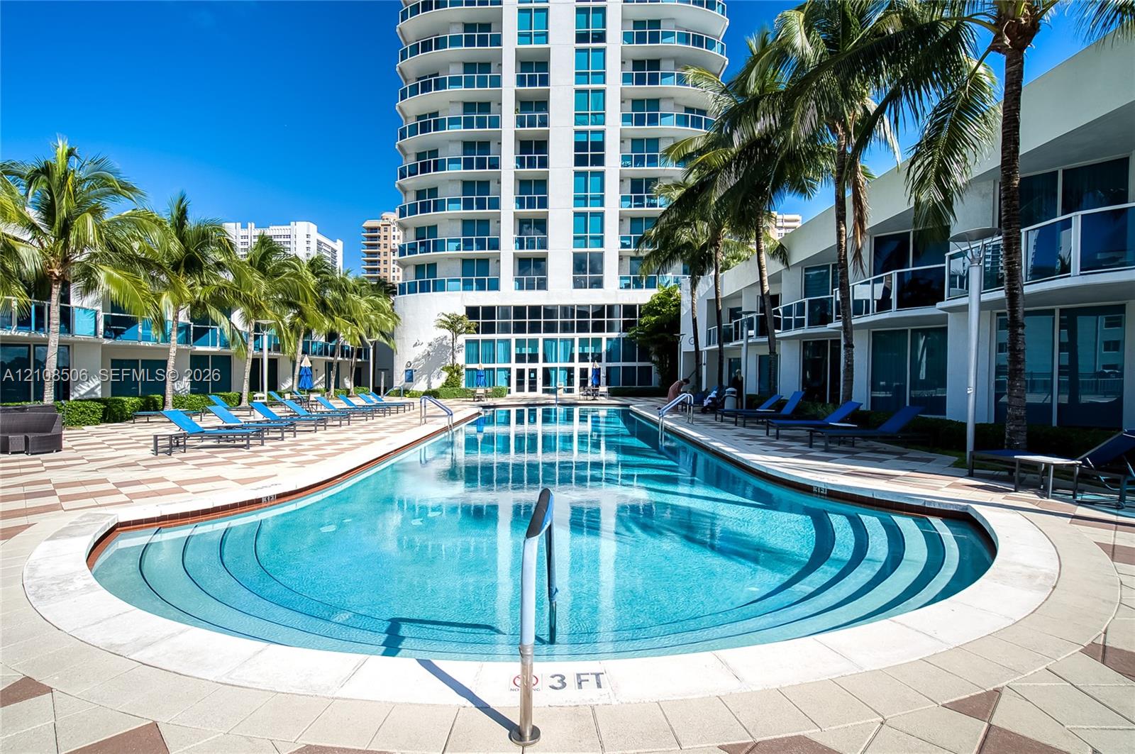 In-ground swimming pool with multi-level entry steps, expansive stone paver deck, and mature palm trees