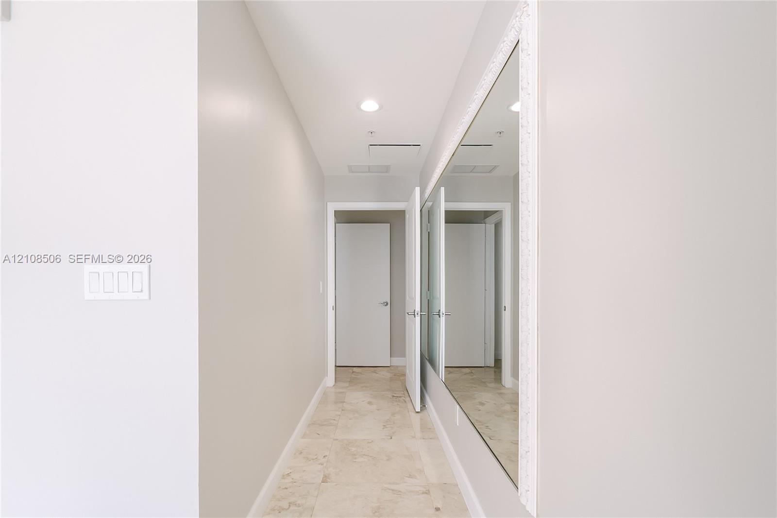 Hallway featuring stone tile flooring, recessed ceiling lighting, and an expansive wall-mounted mirror