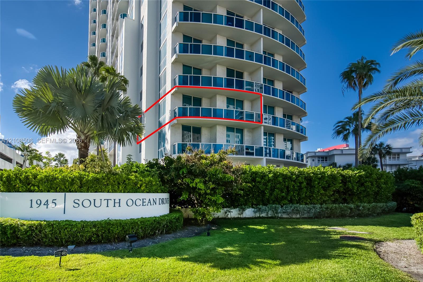 High-rise building exterior featuring tiered concrete balconies with glass railings, large windows, and manicured landscaping