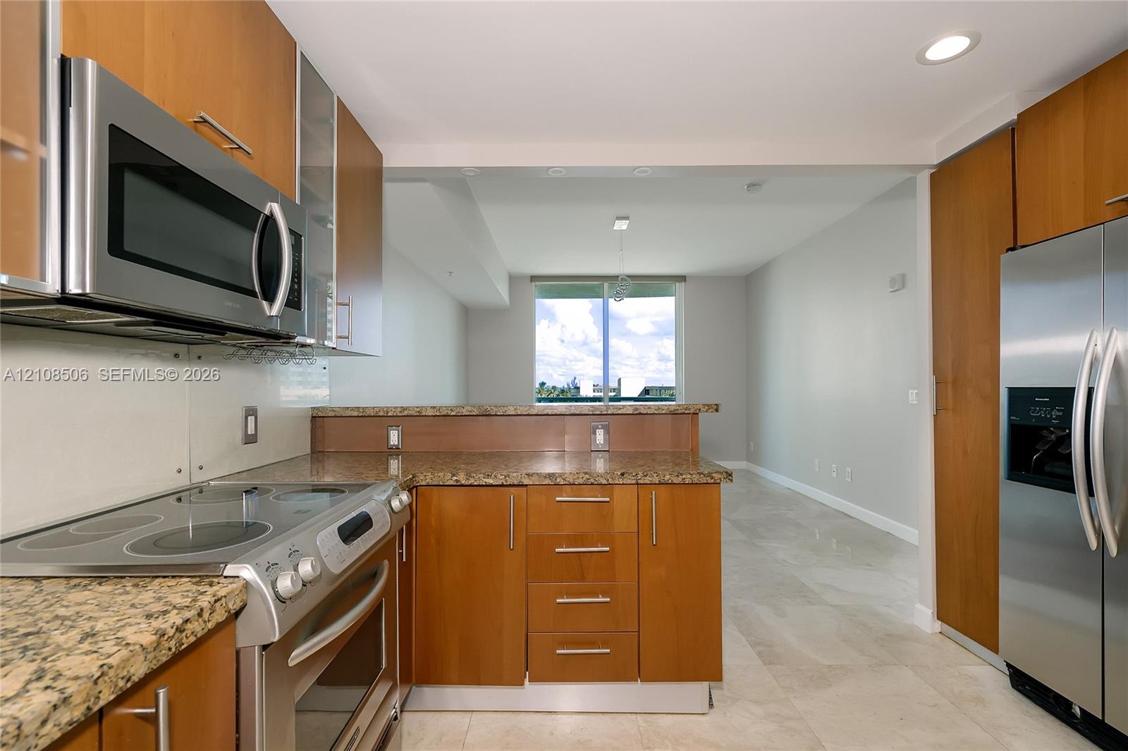 Kitchen featuring wood-veneer cabinetry, stone-finish countertops, stainless steel appliances, and large-format tile flooring