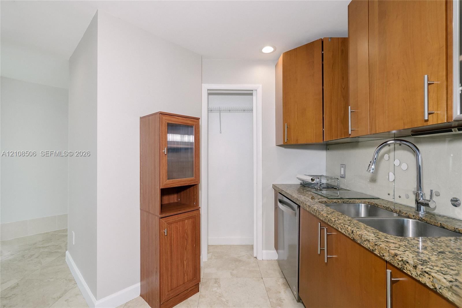 Kitchen area featuring wood cabinetry, stone countertops, double-basin undermount sink with a gooseneck faucet, stainless steel dishwasher, and tile flooring