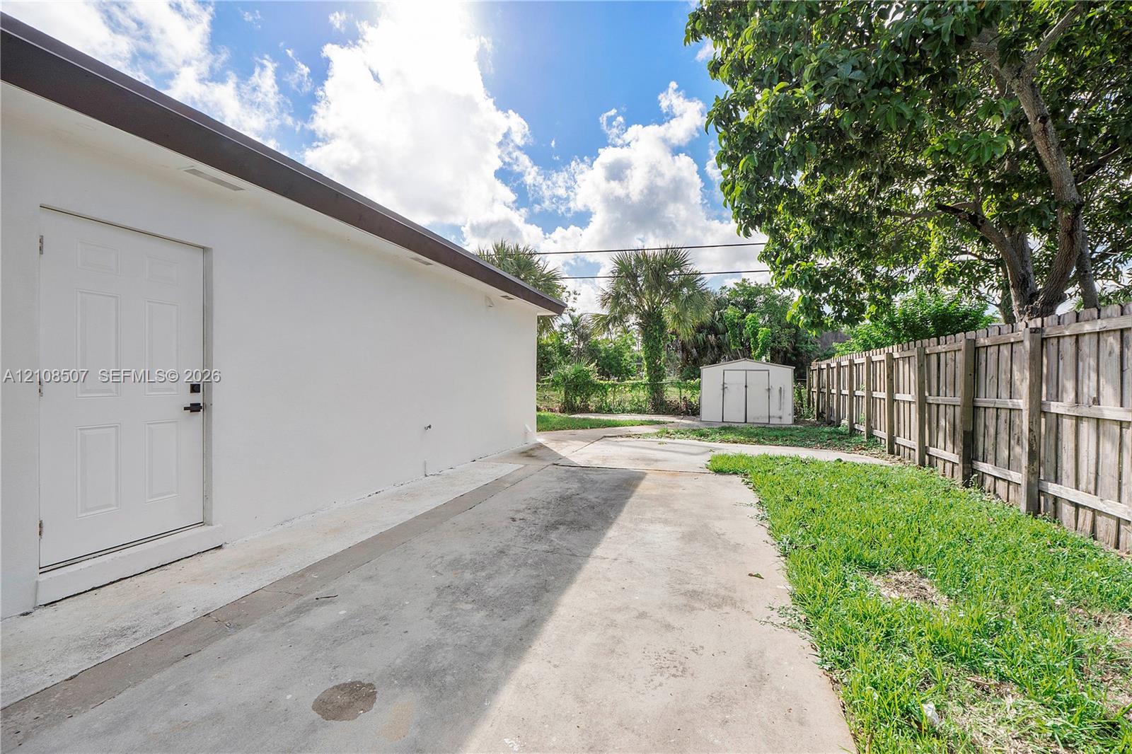 Exterior area featuring a concrete side patio, wood-slat privacy fencing, a storage shed, and mature trees