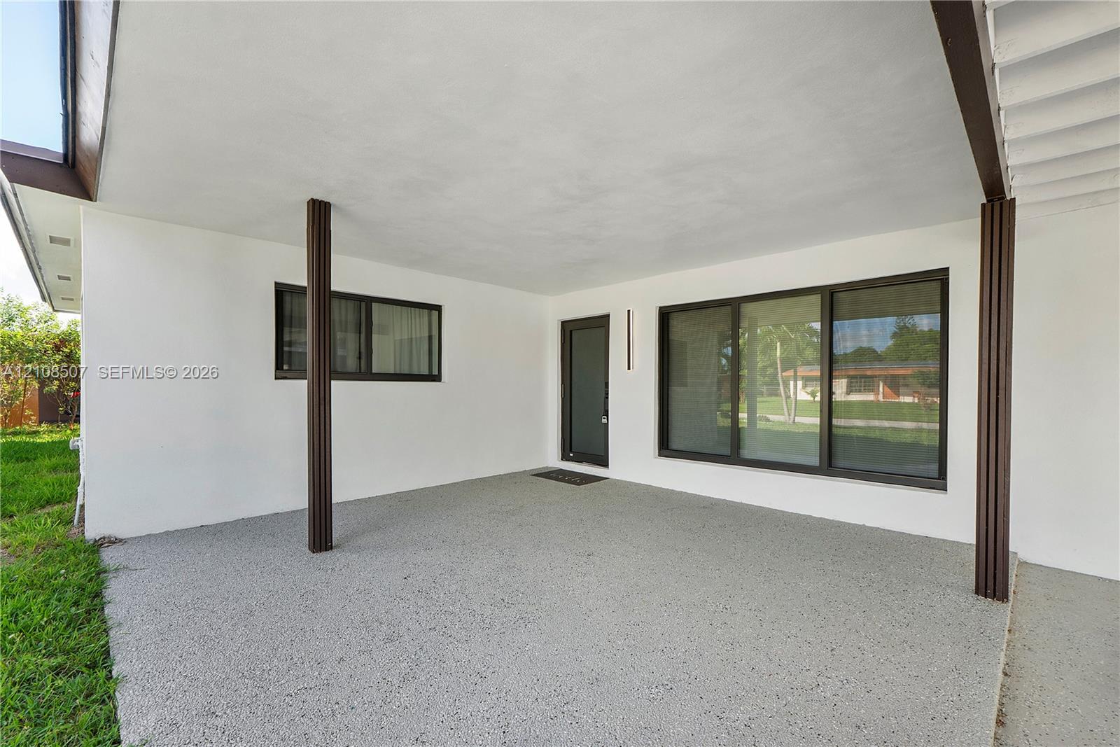 Covered patio featuring an aggregate concrete floor, dark-finished structural support columns, a glass-panel entry door, and large-format multi-pane windows with dark frames