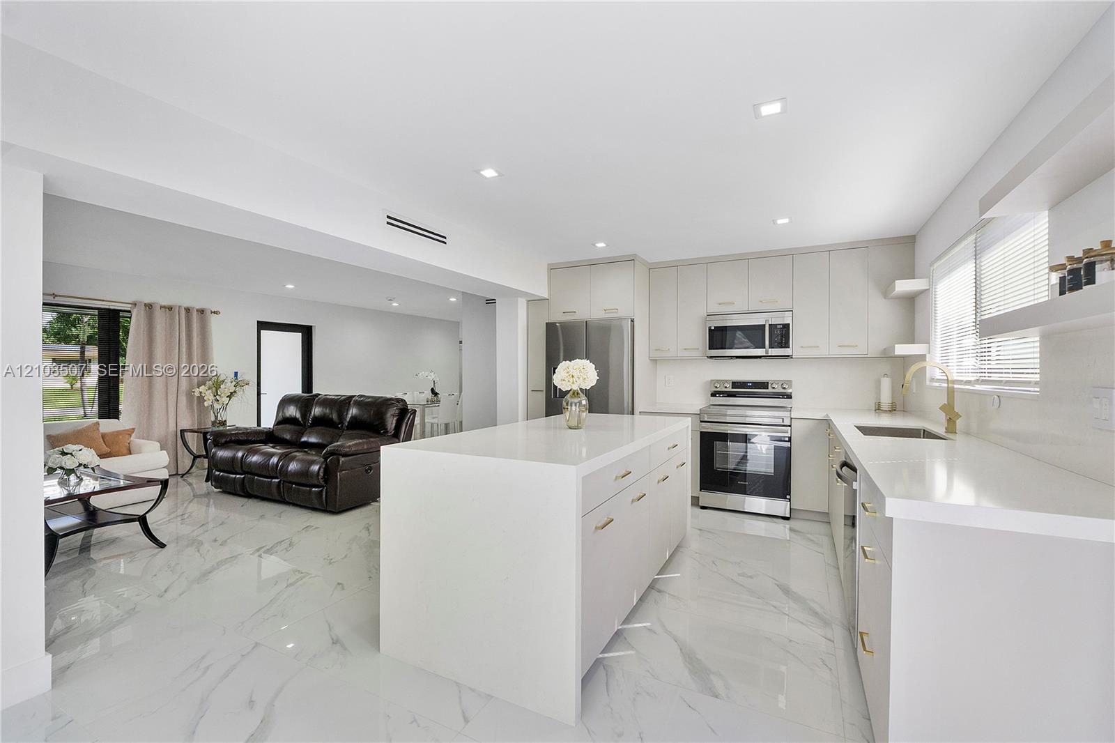 Kitchen featuring a central island with a solid-surface countertop, flat-panel cabinetry, stainless steel appliances, and large-format porcelain tile flooring