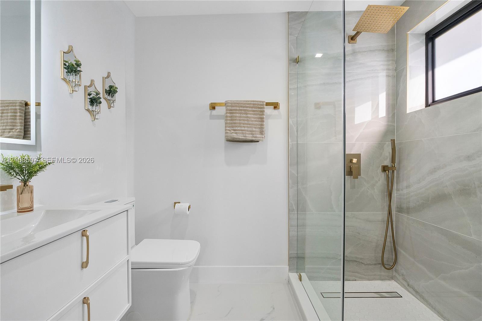 Bathroom featuring a white vanity with gold-tone hardware, large-format tiled walk-in shower with a rain-style showerhead, and matching gold-tone fixtures