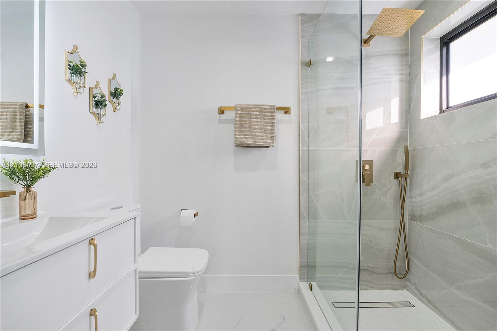 Floating vanity with integrated sink, brass hardware, walk-in shower with glass enclosure, wall-mounted rainfall showerhead, and tile-surround shower walls
