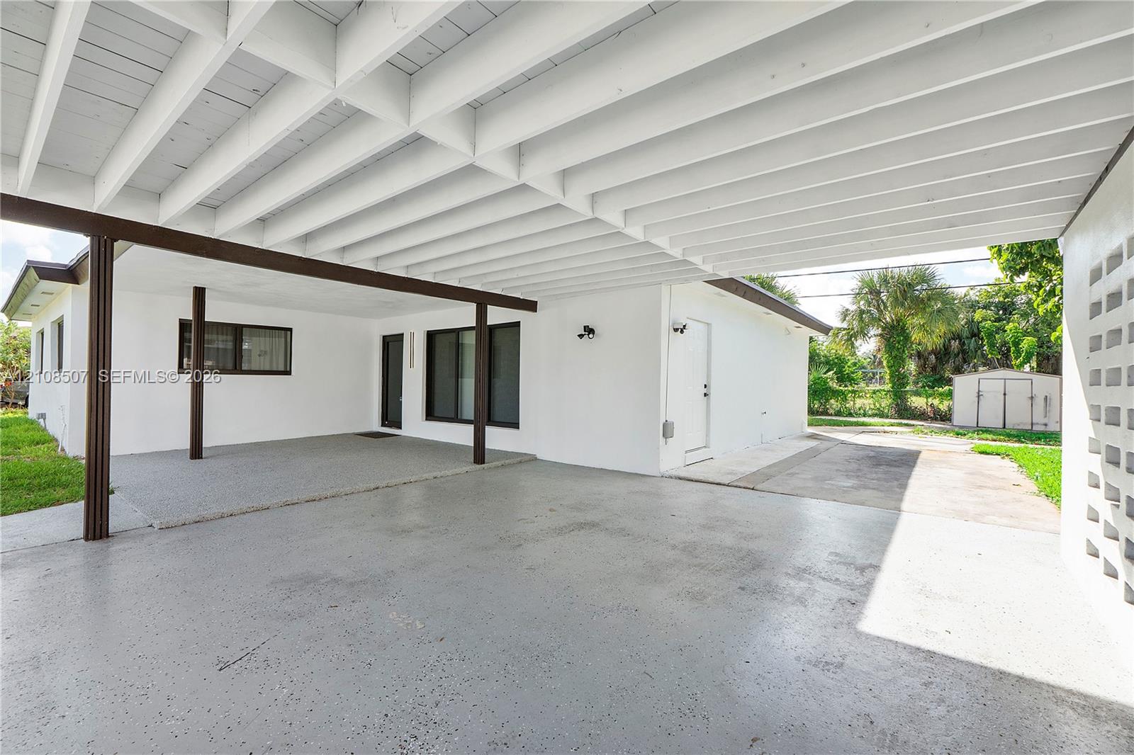 Covered carport featuring an exposed beam ceiling, smooth-finish concrete flooring, and a decorative concrete block privacy screen