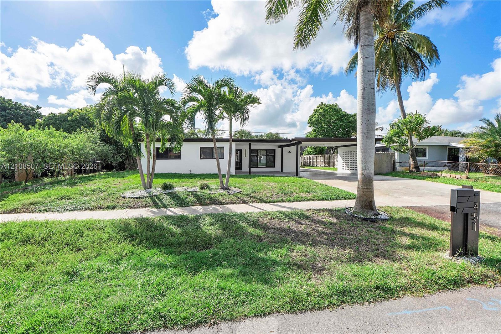 Mid-century modern exterior featuring a flat roofline, white smooth-finish siding, integrated carport, decorative screen wall, and mature palms