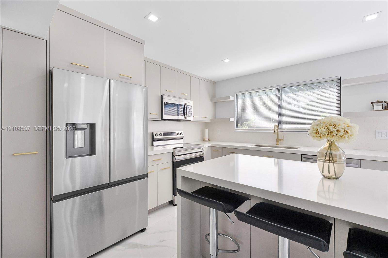Kitchen featuring flat-panel cabinetry with gold-tone hardware, a central island with a solid-surface countertop, stainless steel appliances, and recessed lighting