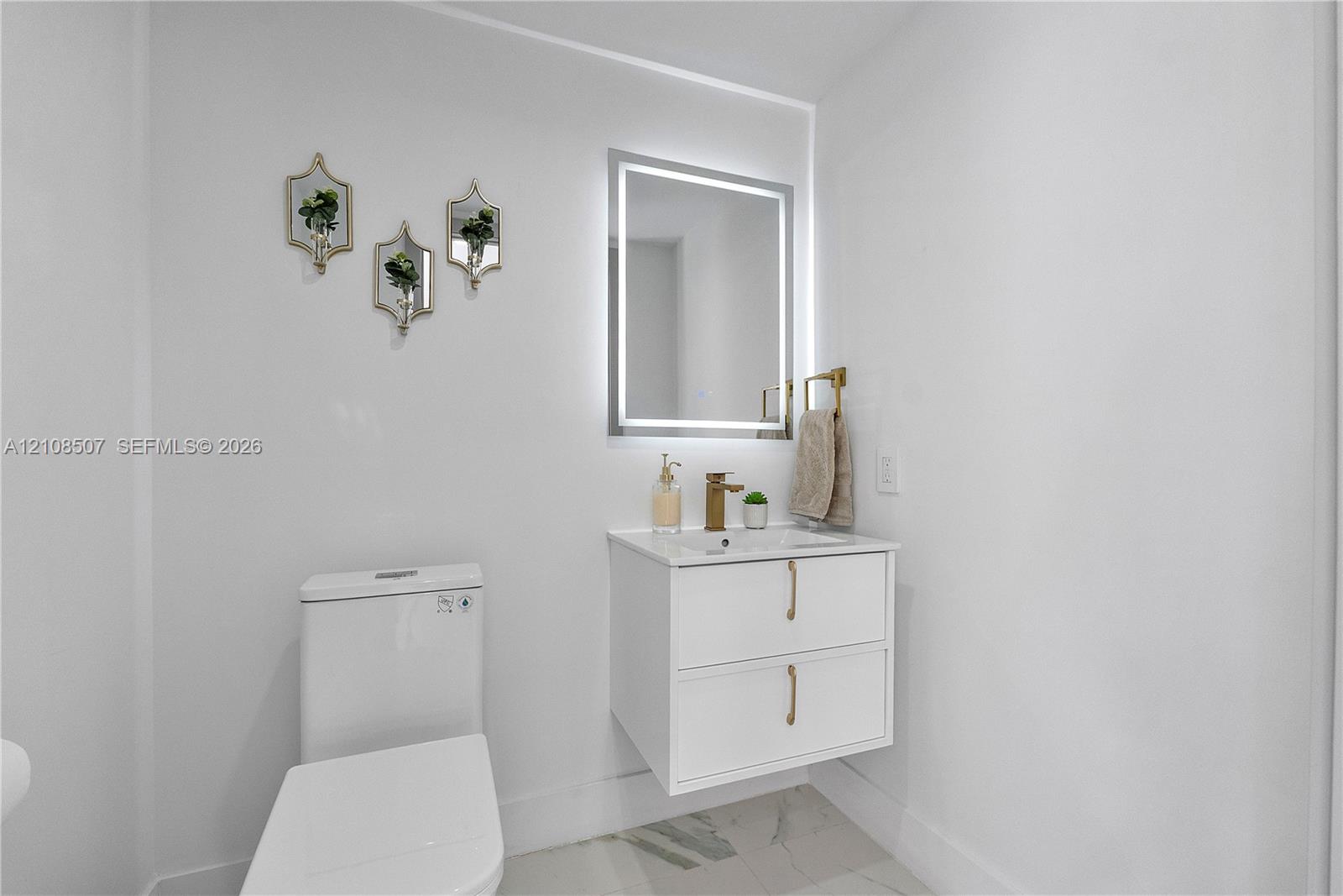 Floating white vanity with double drawers, metallic hardware, integrated stone countertop, LED-backlit mirror, and gold-finish faucet