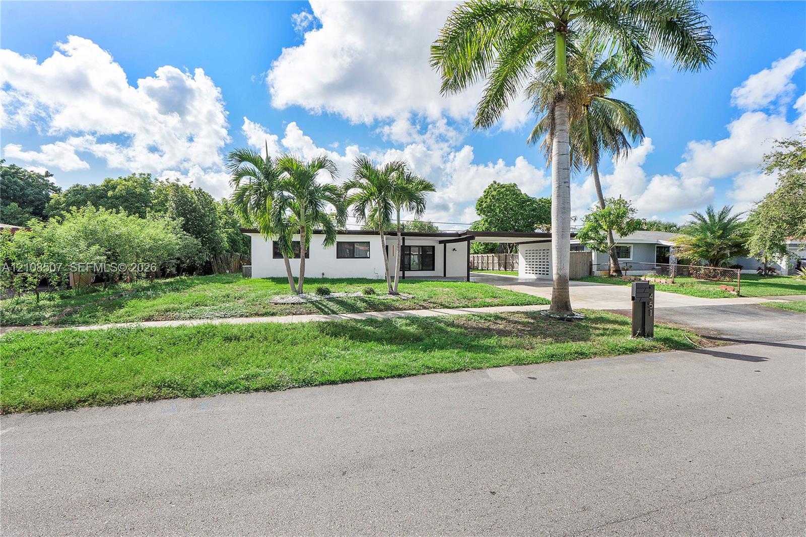 Single-story residence featuring a white stucco exterior, attached carport with decorative breeze block screen, concrete driveway, and mature palm trees