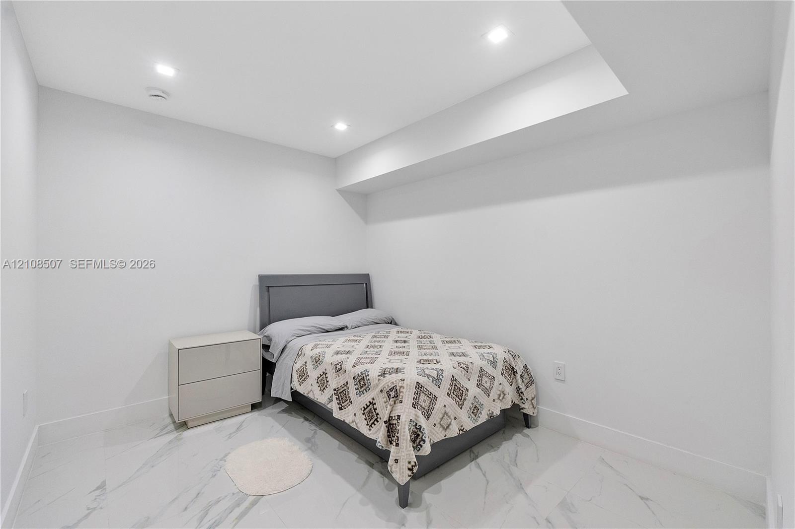 Neutral-toned interior space featuring light-colored stone-finish tile flooring, recessed ceiling lighting, and a recessed ceiling architectural detail