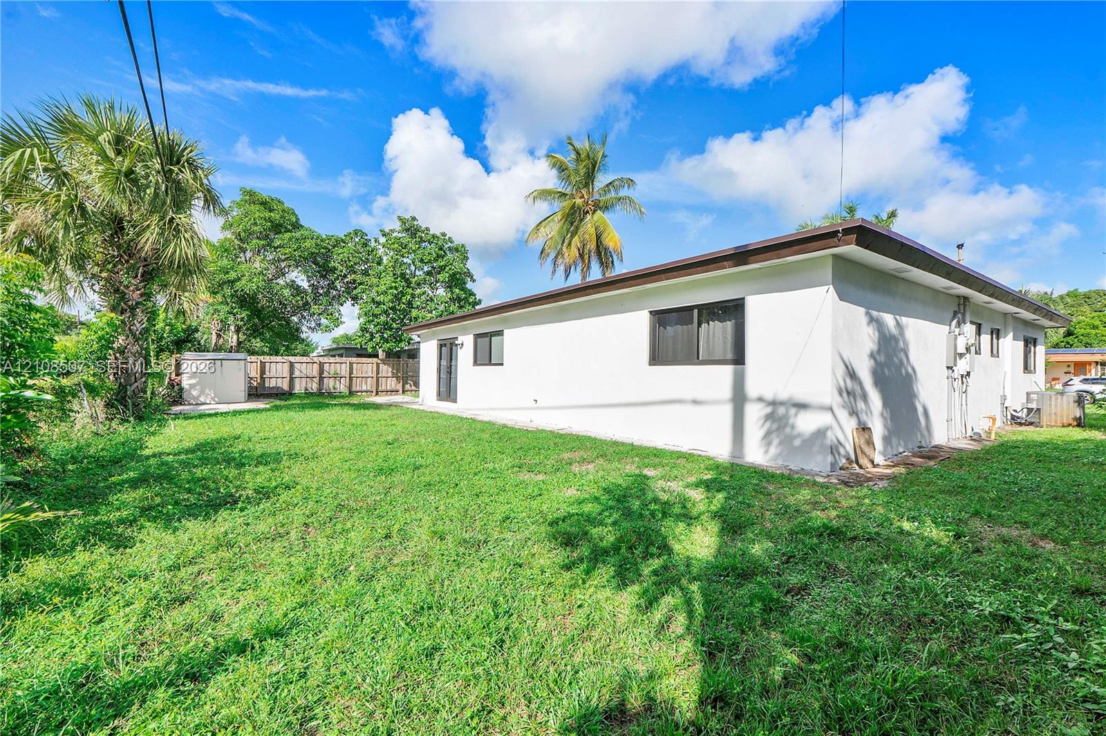 Expansive backyard featuring a large grass lawn, mature palm trees, and perimeter wood fencing