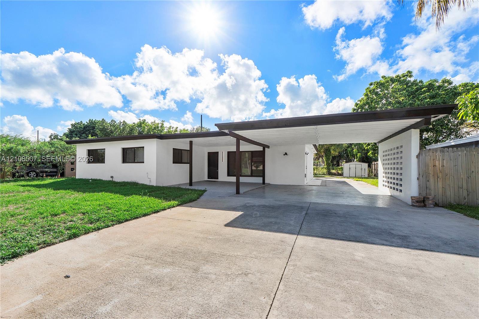 Single-story residence featuring a smooth stucco exterior, attached flat-roof carport, decorative concrete block screening, and an expansive concrete driveway