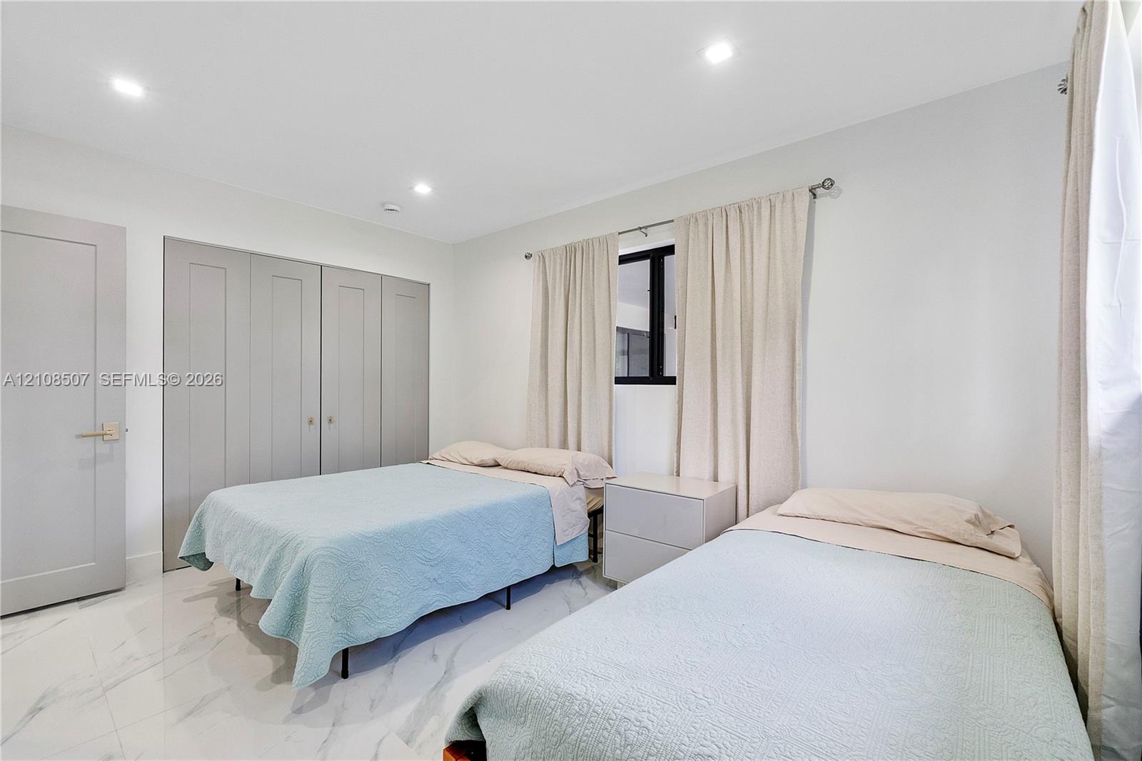Bedroom featuring large-format light-toned tile flooring, recessed ceiling lighting, and built-in shaker-style closet cabinetry with neutral hardware