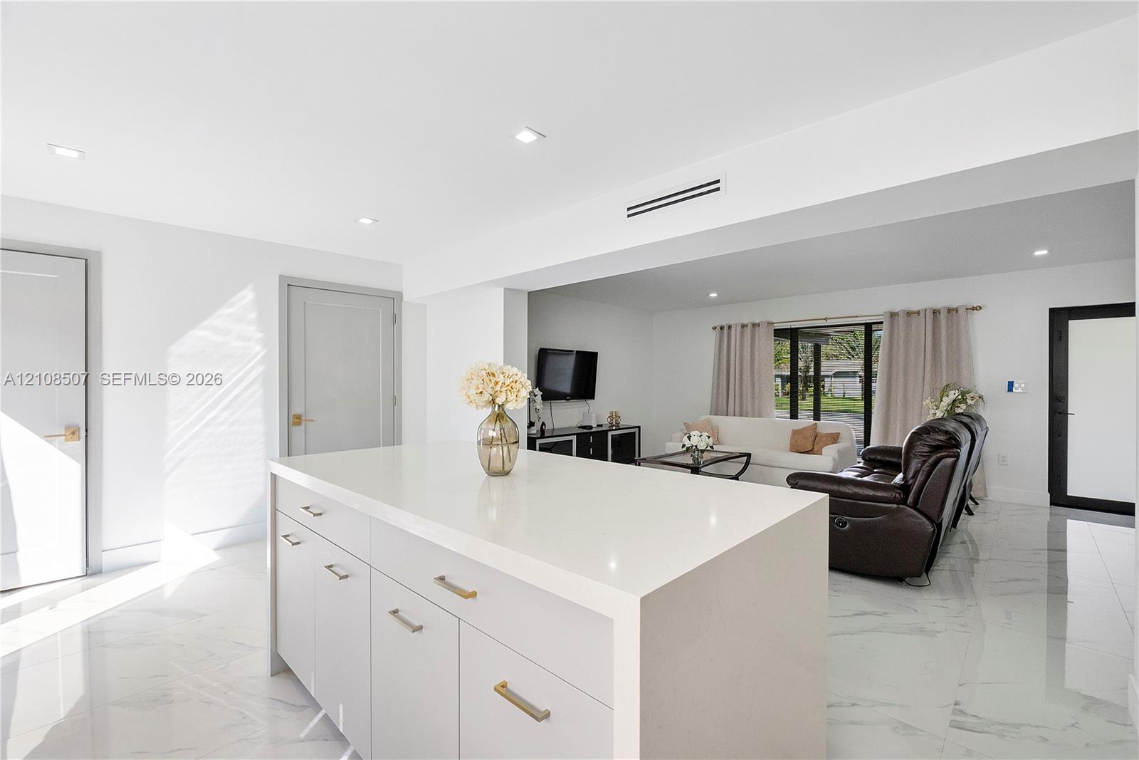 Center island featuring a white stone-surface countertop, recessed ceiling lighting, light-toned cabinetry with metallic hardware, and white tile flooring