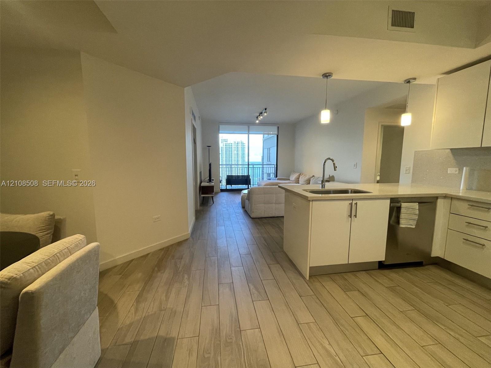 Kitchen featuring white cabinetry, solid-surface countertops, and stainless steel dishwasher, with wood-finish flooring throughout the space and floor-to-ceiling glass paneling