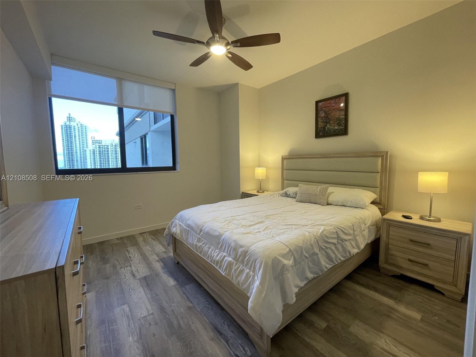 Wood-finish flooring, large-format window with roller shade, and ceiling-mounted fan with integrated lighting