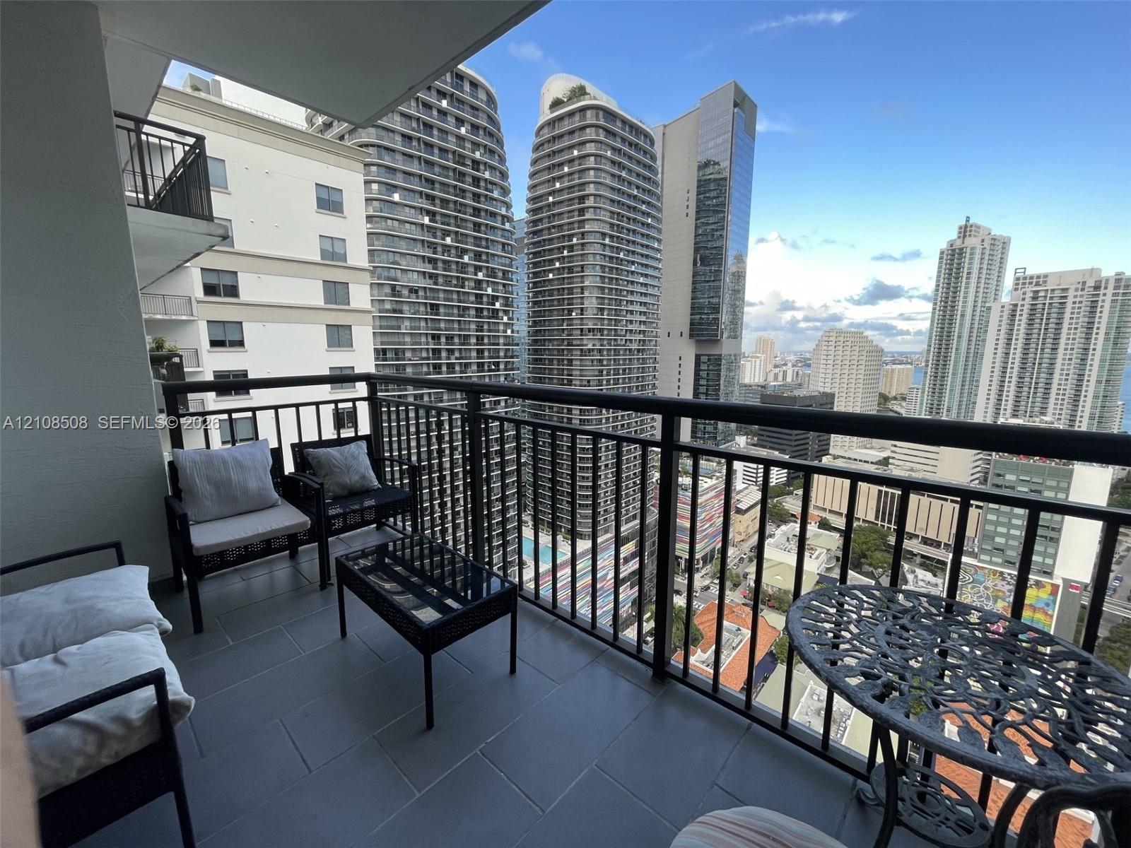 Covered balcony featuring dark-tiled flooring and a black metal railing overlooking an urban cityscape
