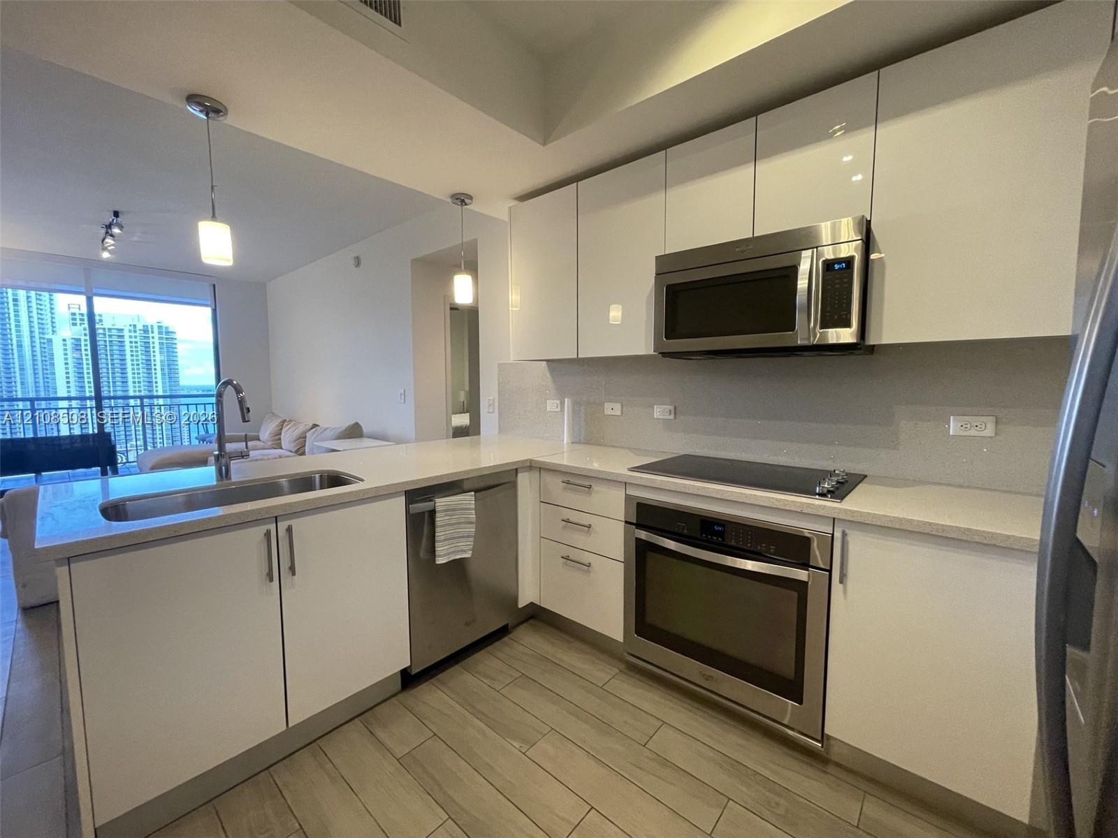 Kitchen featuring high-gloss white cabinetry, stone-finish countertops, stainless steel appliances, and wood-finish flooring